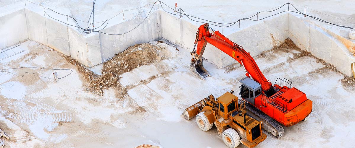 cantera de marmol vista desde arriba con una excavadora roja y otra naranja  en el fondo